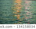 Reflection of city light on water at night. Night sea view with street light. Light hitting on the ocean.Sea background. Background of the calm water, water waves. Sea water surface. 134158034