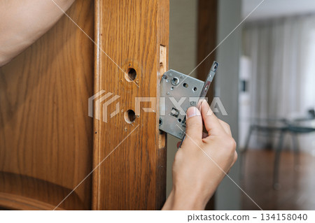 Handyman installing new door lock mechanism into wooden door frame, performing essential repair and maintenance, enhancing home security and functionality during home improvement project. 134158040