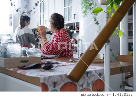The girl has breakfast in the kitchen in the morning at the table in the company of her mother, morning preparations The girl has breakfast in the kitchen in the morning at the table in the company of her mother, morning preparations 134158132