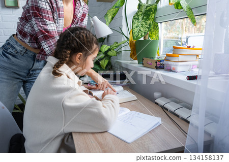 Mom helps and checks a schoolgirl's homework for school at the table Mom helps and checks a schoolgirl's homework for school at the table 134158137