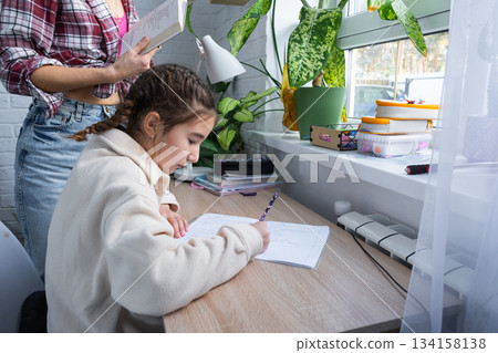 Mom helps and checks a schoolgirl's homework for school at the table 134158138