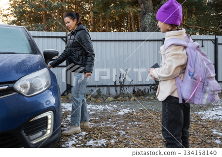 Mom accompanies and puts a schoolgirl girl with a backpack in the car to take her to school 134158140