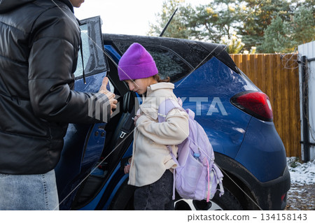 Mom accompanies and puts a schoolgirl girl with a backpack in the car to take her to school Mom accompanies and puts a schoolgirl girl with a backpack in the car to take her to school 134158143