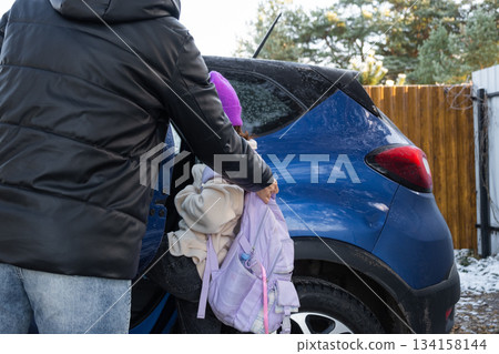 Mom accompanies and puts a schoolgirl girl with a backpack in the car to take her to school Mom accompanies and puts a schoolgirl girl with a backpack in the car to take her to school 134158144