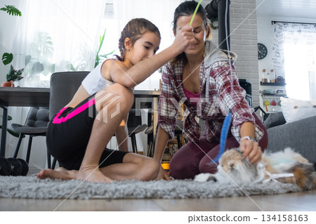 Daughter and mom have fun playing with a pet cat on the carpet 134158163