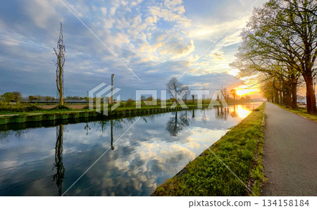 A beautiful scenic sunset reflection can be seen over a calm canal surrounded by lush greenery A beautiful scenic sunset reflection can be seen over a calm canal surrounded by lush greenery 134158184