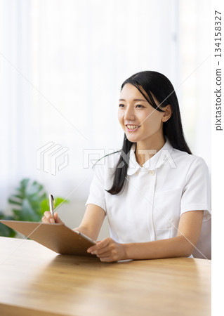 A woman in a white coat smiling and talking while taking notes 134158327