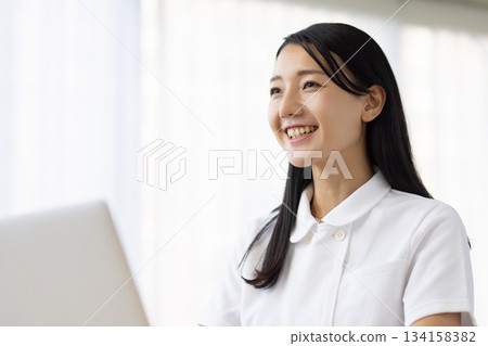 一位身穿白大褂的女士一邊操作電腦一邊微笑著交談。 134158382