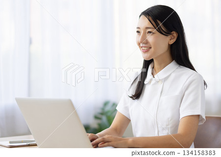 A woman in a white coat smiling and talking while operating a computer 134158383