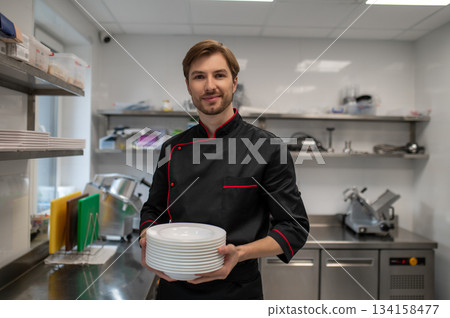 Professional chef holding stack of plates in restaurant kitchen Professional chef holding stack of plates in restaurant kitchen 134158477