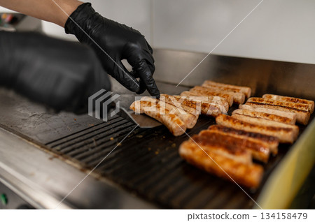 Chef grilling bratwurst sausages on flat-top griddle Chef grilling bratwurst sausages on flat-top griddle 134158479