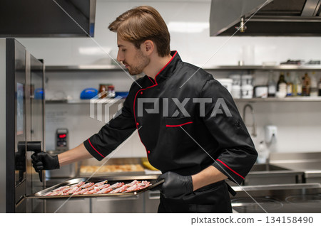Chef placing tray of sliced bacon into commercial oven 134158490