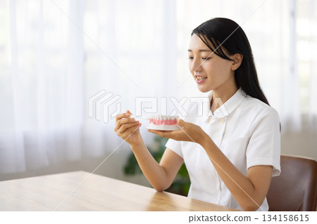 一位身穿白大褂的女士面帶微笑，一邊交談，一邊拿著牙齒模型和牙刷。 134158615