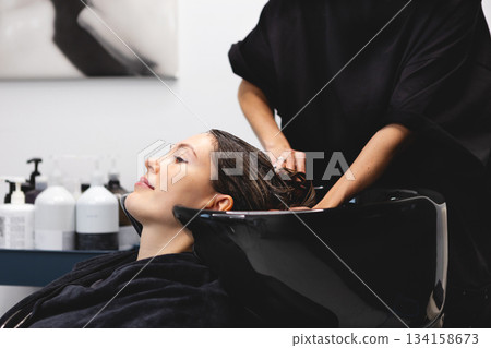 Hairdresser washing womans hair in black salon sink, creating professional beauty care moment inside modern hair studio 134158673