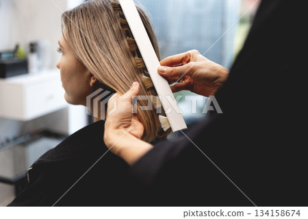 Hairdresser checking hair color of woman with professional shade chart in modern beauty salon, assessing tones and highlights with precision during color consultation Hairdresser checking hair color of woman with professional shade chart in modern beauty salon, assessing tones and highlights with precision during color consultation 134158674