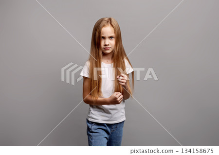 Aggressive young child girl clenching fists in emotional defensive pose, expressing frustration and defiance in studio portrait on gray background, showing intense feelings and reaction Aggressive young child girl clenching fists in emotional defensive pose, expressing frustration and defiance in studio portrait on gray background, showing intense feelings and reaction 134158675