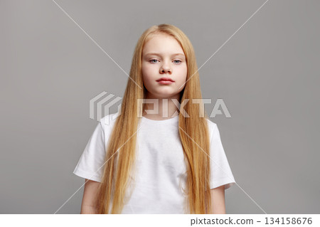 Beauty portrait young blond girl with long straight hair and blue eyes in studio, posing on gray background in modern minimal style. Caucasian Fashion model in white clothing looking at camera 134158676
