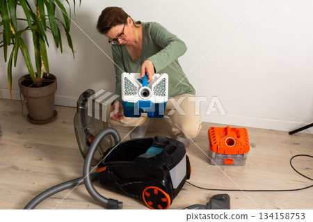 Person getting ready to use a vacuum cleaner in a living room. The person adjusts the vacuum and prepares to clean the floor near a potted plant and cleaning tools Person getting ready to use a vacuum cleaner in a living room. The person adjusts the vacuum and prepares to clean the floor near a potted plant and cleaning tools 134158753