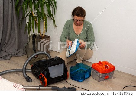 A person is getting ready to vacuum a room. They are attaching a container to the vacuum cleaner while kneeling on the floor. A plant is visible in the background A person is getting ready to vacuum a room. They are attaching a container to the vacuum cleaner while kneeling on the floor. A plant is visible in the background 134158756