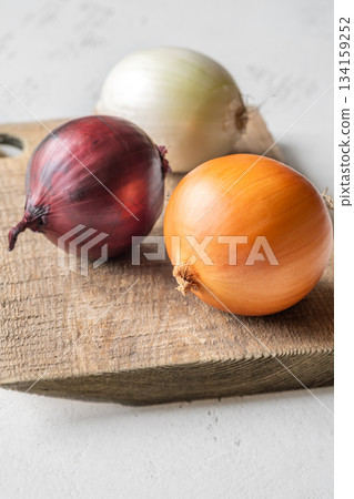 Three whole onions on rustic board showing red, yellow, and white varieties 134159252