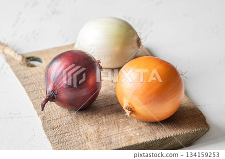 Three whole onions on rustic board showing red, yellow, and white varieties 134159253