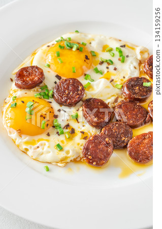 Hearty fried eggs served with caramelized chorizo slices and fresh scallion garnish 134159256