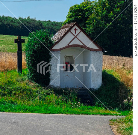 Old stone chapel with bell gable and tiled roof in green field under cloudy sky 134159264