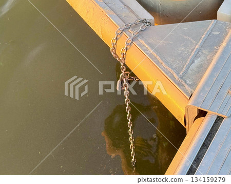 Spider web on metal boat frame with thick chain above brown lake water on sunny summer day 134159279