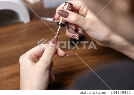 Young woman applying brown gel nail polish on her fingernail, demonstrating at-home manicure for personal beauty, self-care, and relaxation Young woman applying brown gel nail polish on her fingernail, demonstrating at-home manicure for personal beauty, self-care, and relaxation 134159421
