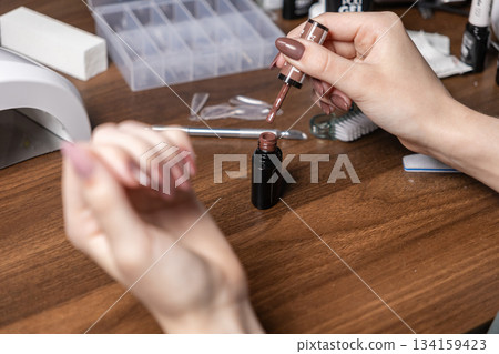 Woman performing her own personal manicure, carefully holding brown gel polish brush, demonstrating at-home self-care, beauty, and creative nail art Woman performing her own personal manicure, carefully holding brown gel polish brush, demonstrating at-home self-care, beauty, and creative nail art 134159423
