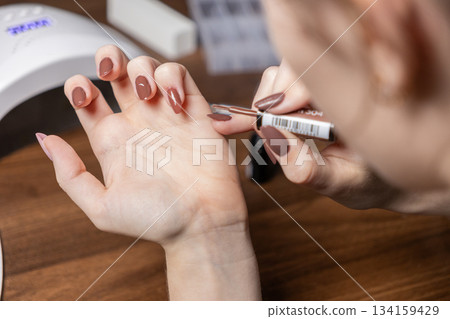 Young woman meticulously applying trendy brown gel nail polish to her own hands, symbolizing personal beauty, self-care, and modern DIY home manicure experience Young woman meticulously applying trendy brown gel nail polish to her own hands, symbolizing personal beauty, self-care, and modern DIY home manicure experience 134159429