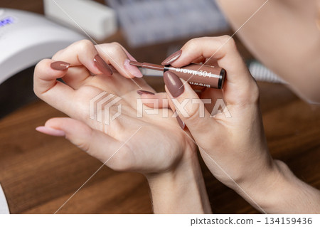 Woman's hands meticulously applying brown nail polish for a self-manicure, reflecting a personal care and relaxing at-home beauty routine with new color Woman's hands meticulously applying brown nail polish for a self-manicure, reflecting a personal care and relaxing at-home beauty routine with new color 134159436