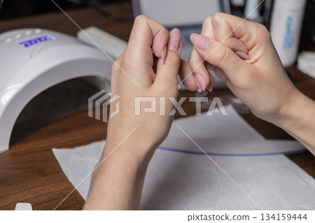 Woman carefully performing her own home manicure, diligently filing natural-looking light pink gel nails, emphasizing personal beauty, self-care, and grooming 134159444