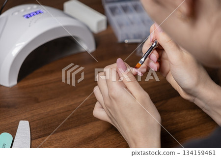 Woman applying builder gel on her fingernail with a brush, performing precise self-manicure for personal beauty and care at home 134159461