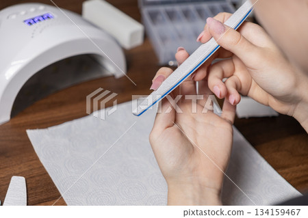Young woman filing her nails with a long nail file, performing a DIY manicure at home, emphasizing personal beauty care and a self-grooming routine 134159467