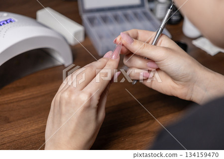 Woman's hands carefully applying a clear upper form for a DIY gel nail extension, showcasing personal beauty and professional home manicure with specialized tools 134159470
