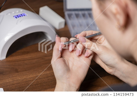 Woman's hands applying clear gel to an artificial nail tip during a personal manicure by oneself at home, showcasing DIY beauty and self-care Woman's hands applying clear gel to an artificial nail tip during a personal manicure by oneself at home, showcasing DIY beauty and self-care 134159473