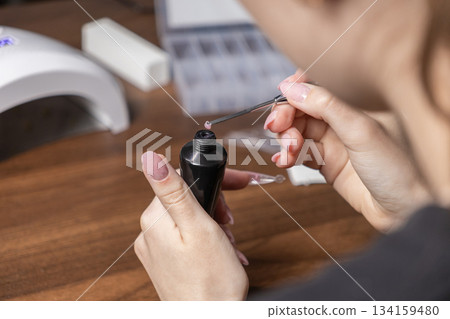 Woman's hands expertly squeezing light pink polygel from a black tube with a spatula tool for a precise self-manicure, demonstrating popular at-home beauty Woman's hands expertly squeezing light pink polygel from a black tube with a spatula tool for a precise self-manicure, demonstrating popular at-home beauty 134159480