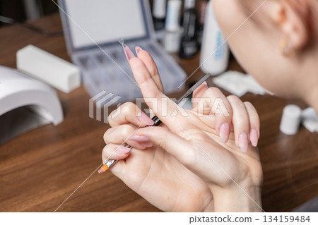 Woman carefully applying gel to a nail extension upper form, showcasing a detailed DIY home manicure process with modern beauty tools Woman carefully applying gel to a nail extension upper form, showcasing a detailed DIY home manicure process with modern beauty tools 134159484