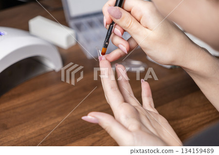 Woman performing a self-manicure, precisely applying nail gel with a brush onto an upper form for trendy nail extensions at her home salon Woman performing a self-manicure, precisely applying nail gel with a brush onto an upper form for trendy nail extensions at her home salon 134159489