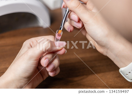 Woman applying polygel to a clear nail extension upper form, performing a DIY self-manicure at home for beautiful hands and personal care 134159497