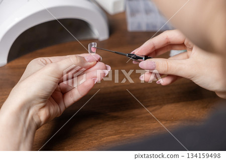 Woman applying pink polygel into a clear upper form for nail extension, performing a modern DIY manicure by herself for personal beauty and self-care Woman applying pink polygel into a clear upper form for nail extension, performing a modern DIY manicure by herself for personal beauty and self-care 134159498