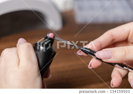 Woman performing a DIY manicure, extracting pink polygel from a tube with a spatula tool for at-home nail extension and personal beauty care Woman performing a DIY manicure, extracting pink polygel from a tube with a spatula tool for at-home nail extension and personal beauty care 134159503