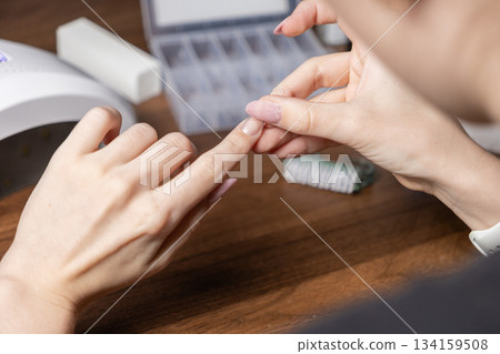 Person carefully applying a clear nail extension upper form to their own finger, performing a detailed DIY manicure for personal beauty and home nail care 134159508