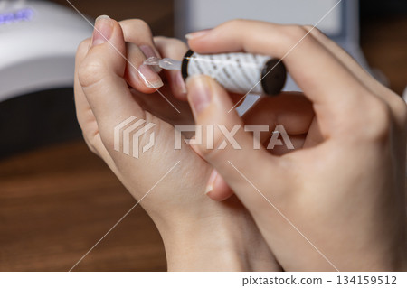 A person skillfully applies a clear gel polish base coat to their fingernail, demonstrating a meticulous self-manicure, promoting home beauty, self-care, and personal wellness 134159512