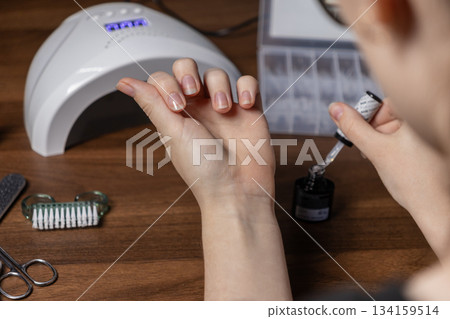 Woman carefully applying clear gel polish to her natural nails with a UV lamp, showcasing a relaxing home manicure by oneself for personal beauty Woman carefully applying clear gel polish to her natural nails with a UV lamp, showcasing a relaxing home manicure by oneself for personal beauty 134159514
