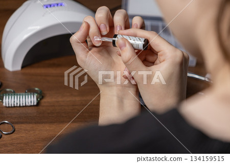 Woman performing a manicure by oneself, applying clear nail polish to her fingernail, promoting self-care, beauty, and personal hygiene at home Woman performing a manicure by oneself, applying clear nail polish to her fingernail, promoting self-care, beauty, and personal hygiene at home 134159515