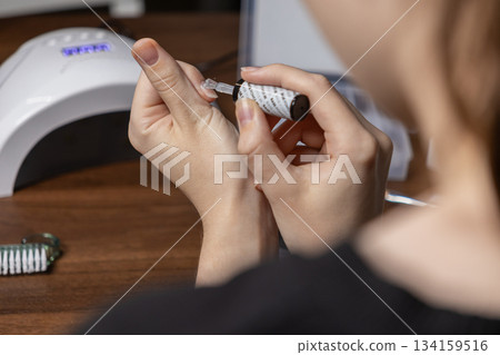 Woman carefully applying clear nail polish to her fingernail by herself, demonstrating a personal home manicure session and beauty self-care routine Woman carefully applying clear nail polish to her fingernail by herself, demonstrating a personal home manicure session and beauty self-care routine 134159516