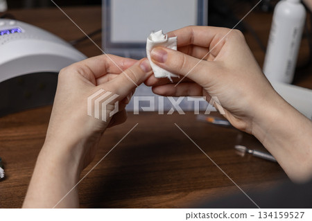 Woman's hands carefully cleaning a fingernail with a white cotton pad, demonstrating meticulous manicure by oneself for personal beauty hygiene 134159527