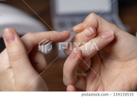 Person's hands holding a clear, flexible nail extension upper form, preparing for a do-it-yourself manicure by oneself or salon beauty 134159535